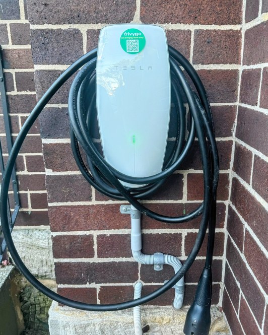 Tesla wall connector on a brick wall with an ivygo QR sticker